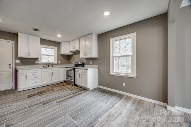 kitchen with white cabinets, light countertops, a sink, and electric range