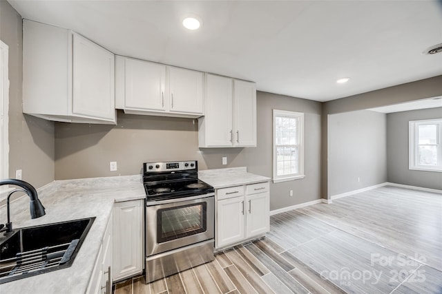 kitchen with wood finish floors, stainless steel electric range oven, light countertops, white cabinetry, and a sink