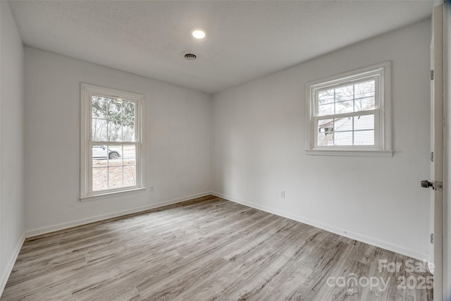 spare room with light wood-type flooring, baseboards, and a textured ceiling