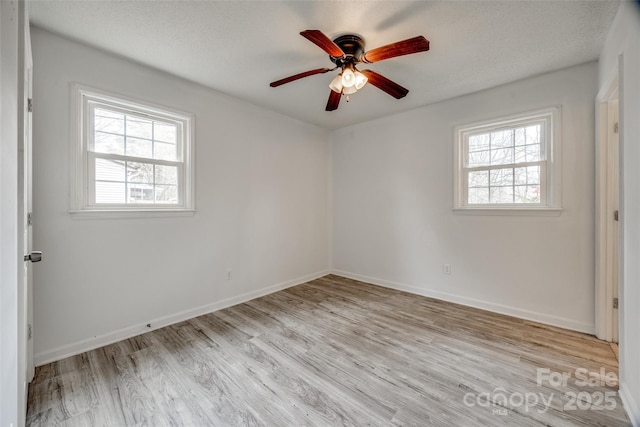 spare room with a healthy amount of sunlight, light wood-style flooring, baseboards, and a textured ceiling