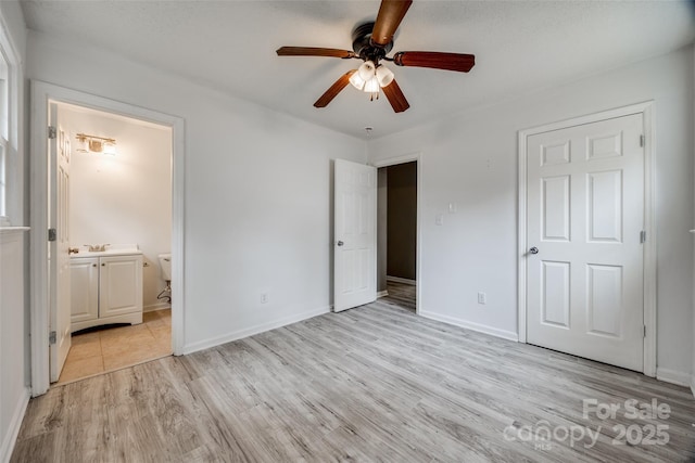 unfurnished bedroom with ceiling fan, a sink, baseboards, light wood-type flooring, and ensuite bath