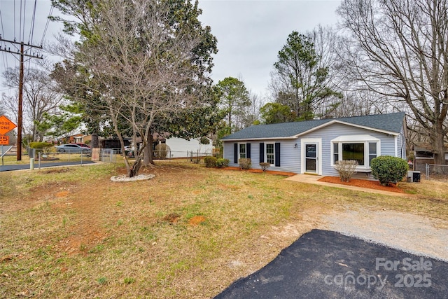 ranch-style home featuring central air condition unit, a shingled roof, fence, and a front yard