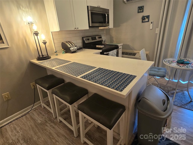 kitchen with a breakfast bar area, stainless steel appliances, tasteful backsplash, white cabinetry, and wood finished floors