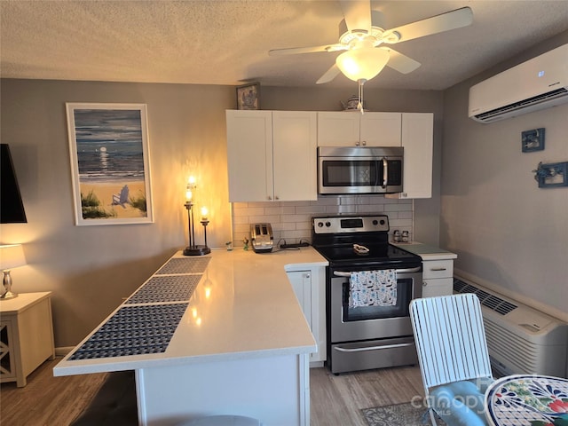 kitchen featuring stainless steel appliances, white cabinetry, light wood-style floors, light countertops, and a wall mounted air conditioner