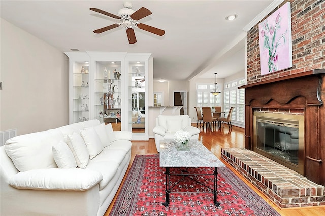 living area featuring visible vents, a fireplace, ceiling fan, and wood finished floors