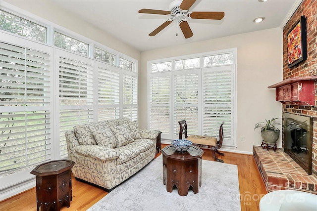 living area with ceiling fan, baseboards, a brick fireplace, and wood finished floors