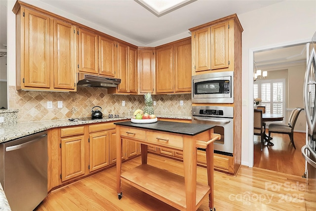 kitchen featuring tasteful backsplash, under cabinet range hood, light wood-style flooring, an inviting chandelier, and stainless steel appliances