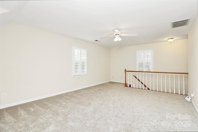 carpeted empty room featuring visible vents, a ceiling fan, and baseboards