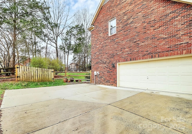 view of side of home featuring brick siding, driveway, an attached garage, and fence