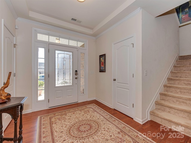 foyer featuring stairs, a tray ceiling, visible vents, and wood finished floors