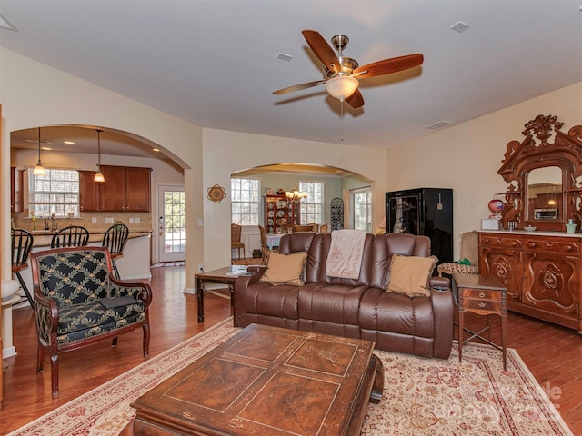 living area with ceiling fan with notable chandelier, arched walkways, visible vents, and wood finished floors