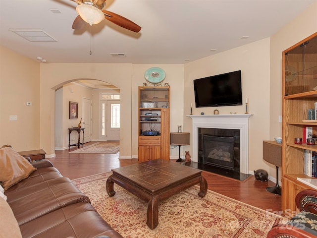 living area with arched walkways, wood finished floors, visible vents, a ceiling fan, and a glass covered fireplace