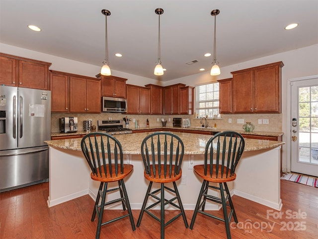 kitchen with appliances with stainless steel finishes, wood finished floors, a sink, and a center island