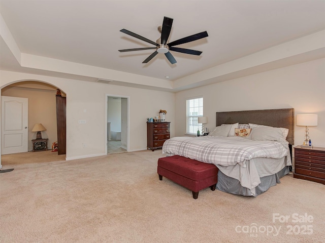 bedroom with a tray ceiling, arched walkways, carpet, a ceiling fan, and baseboards