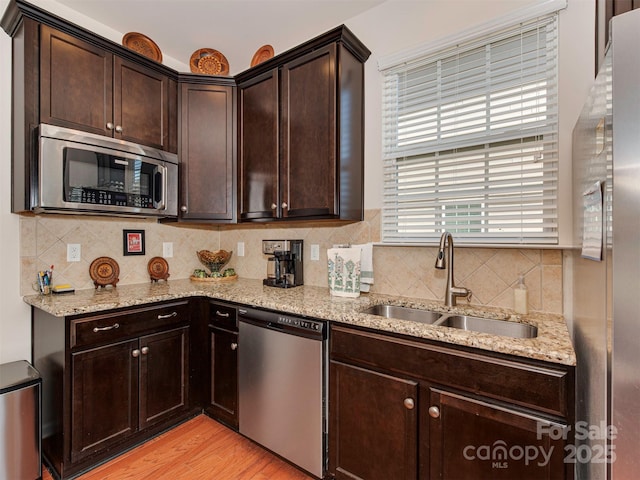 kitchen featuring tasteful backsplash, appliances with stainless steel finishes, light stone counters, dark brown cabinets, and a sink