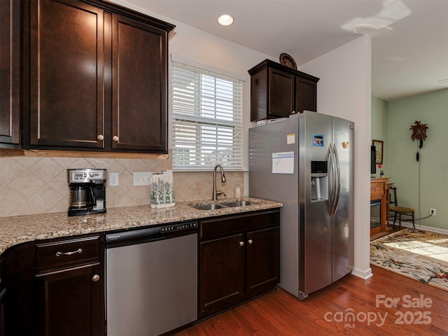 kitchen with dark brown cabinetry, stainless steel appliances, dark wood-type flooring, a sink, and tasteful backsplash