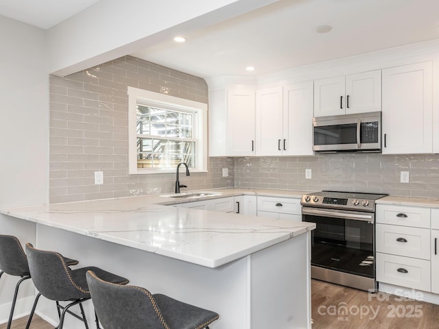 kitchen featuring light wood finished floors, white cabinets, a peninsula, stainless steel appliances, and a sink