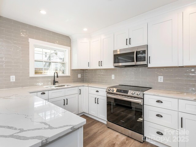 kitchen with light wood finished floors, decorative backsplash, appliances with stainless steel finishes, white cabinets, and a sink