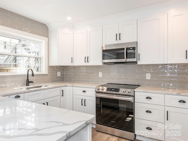 kitchen featuring light stone counters, stainless steel appliances, a sink, white cabinetry, and decorative backsplash