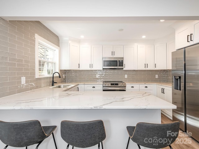 kitchen featuring a peninsula, light stone counters, stainless steel appliances, and a sink