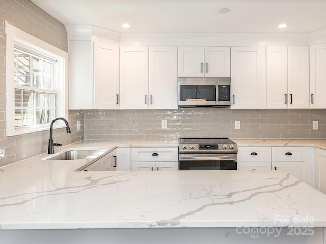 kitchen with appliances with stainless steel finishes, backsplash, a sink, and white cabinetry