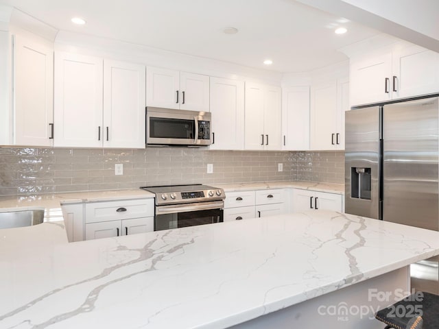 kitchen with light stone countertops, appliances with stainless steel finishes, white cabinets, and decorative backsplash