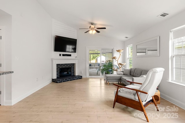 living area with visible vents, a fireplace with raised hearth, a ceiling fan, lofted ceiling, and light wood-type flooring