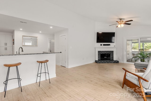 living room featuring lofted ceiling, a fireplace with raised hearth, ceiling fan, visible vents, and light wood finished floors