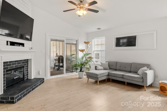 living room featuring ceiling fan, a fireplace, wood finished floors, visible vents, and vaulted ceiling