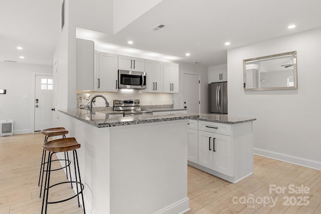 kitchen featuring light wood finished floors, a breakfast bar area, backsplash, appliances with stainless steel finishes, and stone countertops