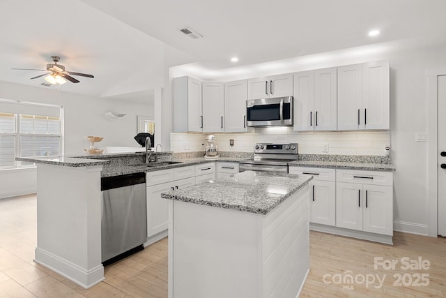 kitchen featuring light stone counters, stainless steel appliances, a sink, visible vents, and tasteful backsplash