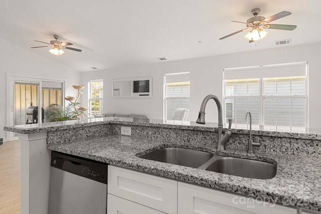 kitchen featuring light stone counters, stainless steel dishwasher, a sink, and visible vents