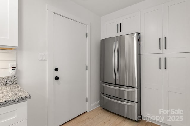 kitchen featuring light wood finished floors, light stone counters, white cabinets, and freestanding refrigerator