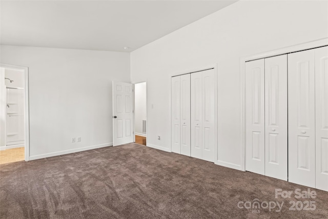 unfurnished bedroom featuring carpet floors, vaulted ceiling, ensuite bathroom, and two closets