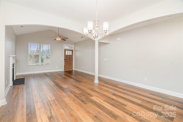 unfurnished living room with arched walkways, lofted ceiling, light wood-style flooring, ceiling fan with notable chandelier, and a fireplace with flush hearth