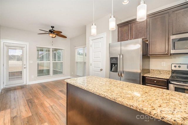 kitchen featuring light wood finished floors, stainless steel appliances, dark brown cabinets, and light stone counters