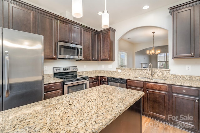 kitchen featuring light stone counters, dark brown cabinetry, stainless steel appliances, a sink, and hanging light fixtures