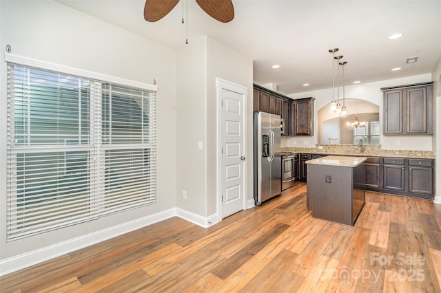 kitchen with stainless steel appliances, arched walkways, dark brown cabinetry, and light wood finished floors