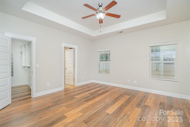 unfurnished bedroom featuring light wood-type flooring, multiple windows, baseboards, and a raised ceiling