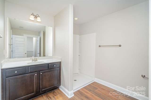 full bathroom featuring wood finished floors, vanity, baseboards, and walk in shower