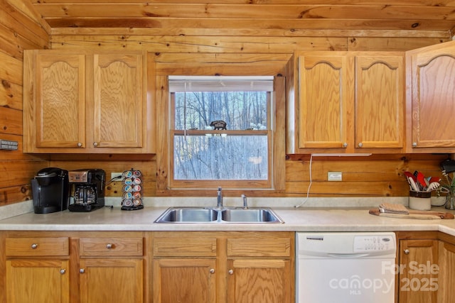 kitchen with wooden walls, dishwasher, light countertops, light brown cabinets, and a sink