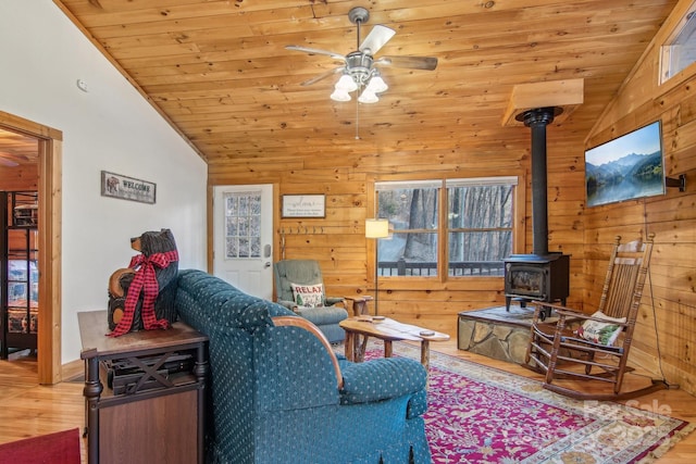 living area featuring a ceiling fan, lofted ceiling, wood finished floors, a wood stove, and wood walls