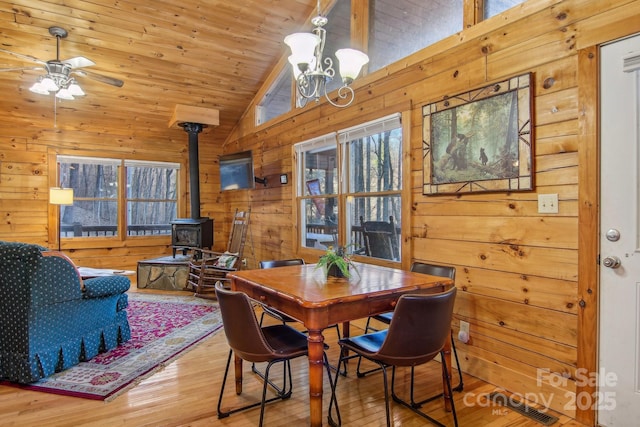 dining space with wooden walls, wood finished floors, wood ceiling, vaulted ceiling, and a wood stove