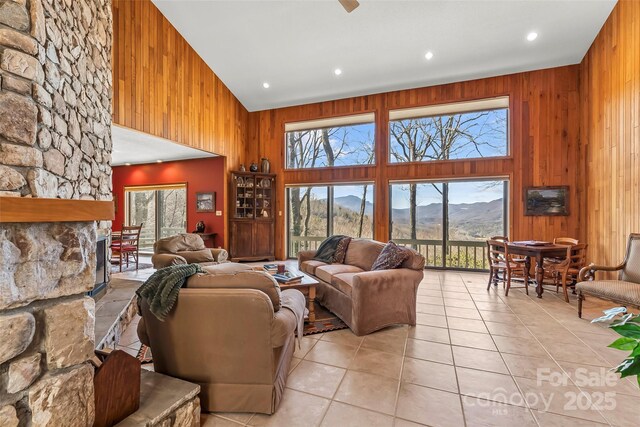 living area with a stone fireplace, light tile patterned floors, a mountain view, wooden walls, and a high ceiling