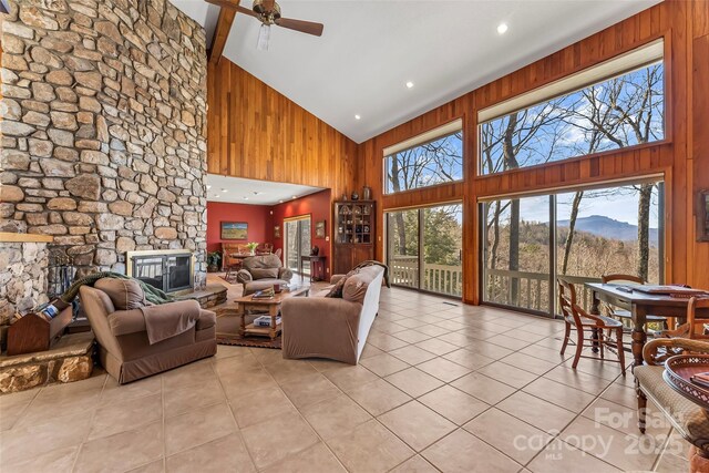 living room with light tile patterned floors, high vaulted ceiling, a stone fireplace, and a healthy amount of sunlight
