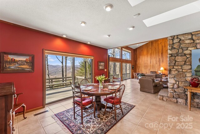 dining room featuring wood walls, light tile patterned floors, a healthy amount of sunlight, and a skylight