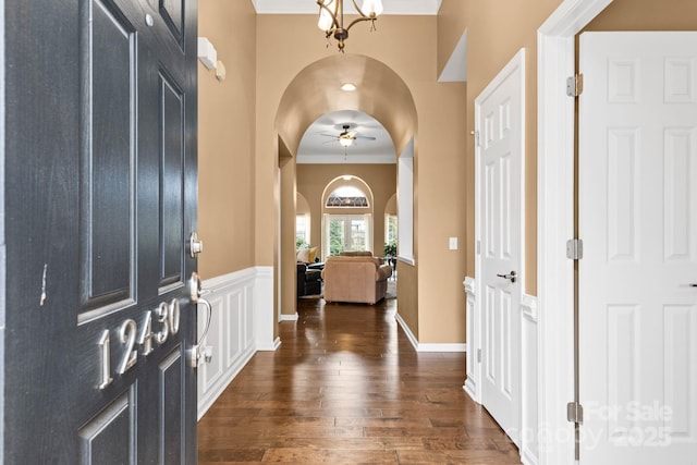 foyer featuring arched walkways, dark wood-type flooring, ceiling fan with notable chandelier, and ornamental molding