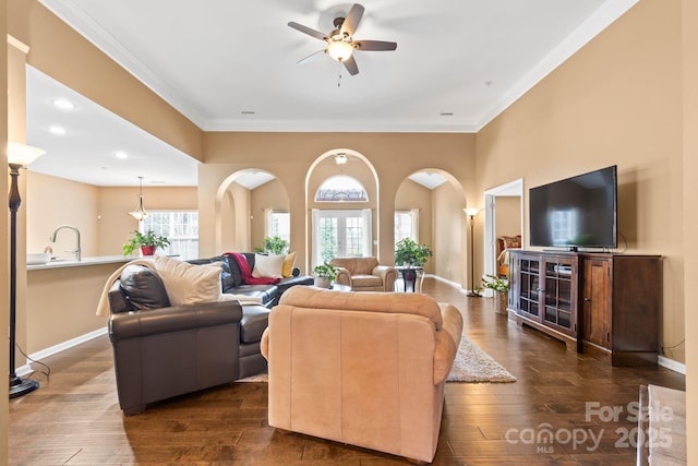 living area with dark wood-style floors, arched walkways, ornamental molding, and baseboards