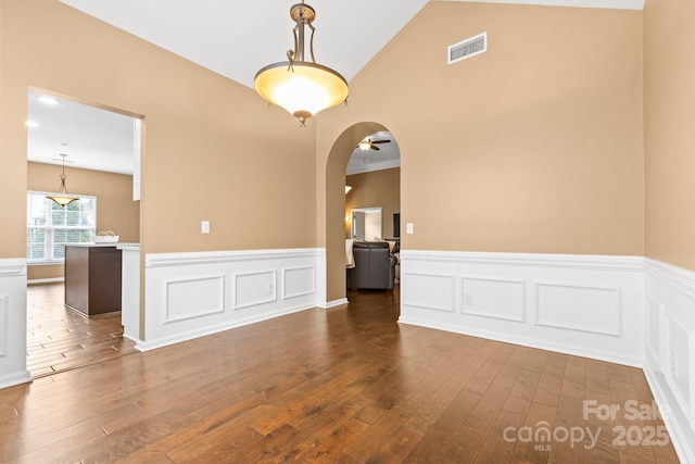 spare room with dark wood-style floors, arched walkways, a wainscoted wall, visible vents, and vaulted ceiling