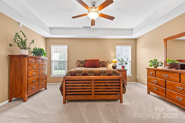 bedroom with ceiling fan, light carpet, visible vents, baseboards, and a raised ceiling